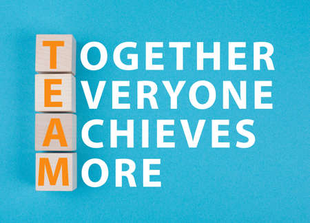 Team, together everyone achieves more is standing on a blue colored background, wooden cubesの写真素材