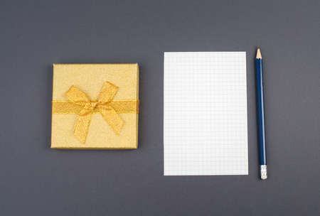 Empty paper, a pen and a golden colored gift on a dark gray background, copy space for textの写真素材