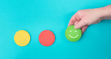 Hand holds a green smiling face, red and yellow circle empty, blue colored background, copy space, customer reviewの写真素材