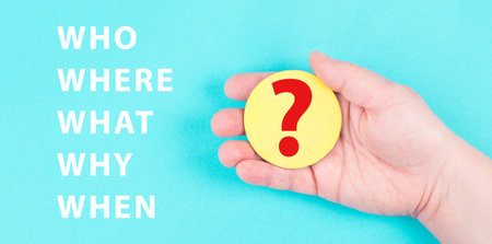 The words who, what, why, when, where are standing on a blue colored background, hand is holding a...