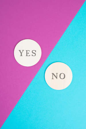 The words yes and no are standing on circular shaped wood, colorful pink and blue background, decision making conceptの写真素材