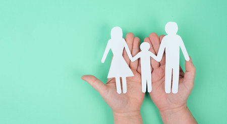 Parents with one child holding hands, paper cut out, copy space, petrol colored background,...