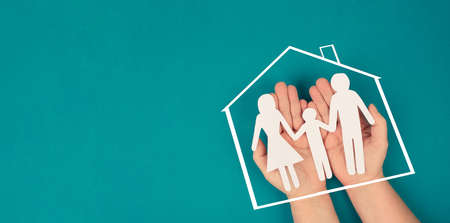 A family, mother, father and child in silhouette, paper cut out, holding in hands, roof of a house, petrol colored backgroundの写真素材
