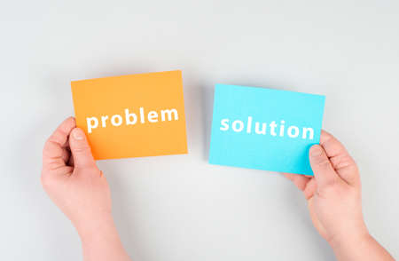 The words problem and solution are standing on orange and blue colored paper, brainstorming for new ideas, hands holding the messageの写真素材