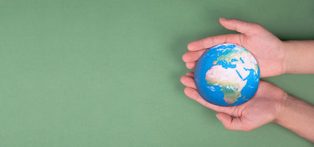 Hands holding planet earth in front of a green background, environmental isuues, copy spaceの写真素材
