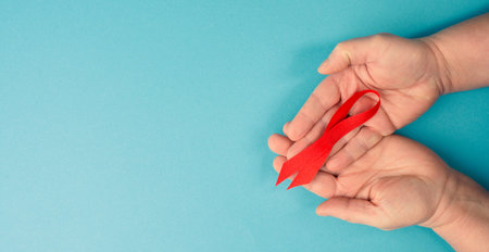 hands holding red AIDS awareness ribbon, blue background with copy space for text