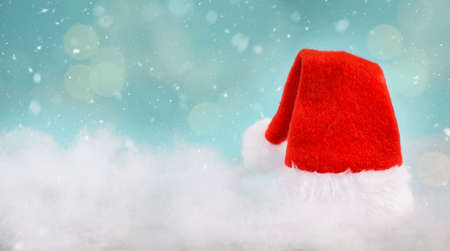 Christmas greeting card with a red hat of Santa Claus, blue colored background with bokeh lights and snowflakesの写真素材
