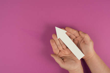 Holding an arrow in the hand, symbol for growth, success and development, pink colored background, copy space for textの写真素材