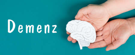 Dementia is standing on a paper, German language, hands holding brain, disease diagnosis, Alzheimer's illness, awardness dayの写真素材