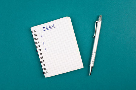 Empty notebook with a pen on a petrol colored background, the word plan is standing on the top of...