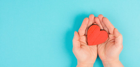 Woman is holding a red heart in her hand, blue colored background, copy space, love and charity...