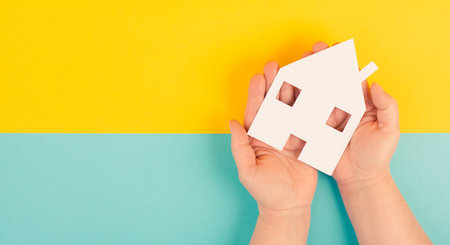 Holding a small paper house in the hands, planning to buy a new home, real estate, owning propertyの写真素材