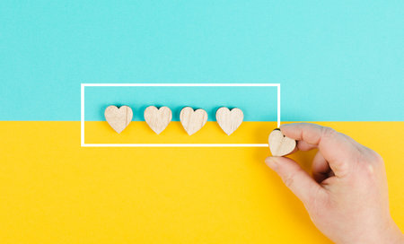 Five hearts on a blue and yellow colored background, hand put the last heart in the row, rating,...