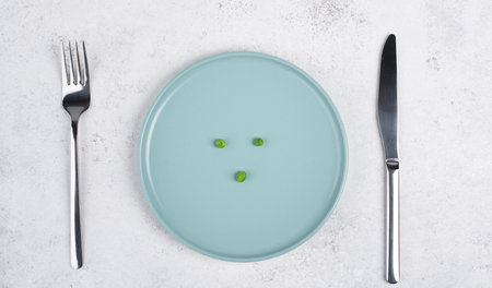 Three green peas on a plate, fork and knife on the table, diet and loosing weight concept, healthy lifestyleの写真素材