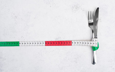 Fork and knife tight together with a tape measure, copy space for text, making a diet, loosing...