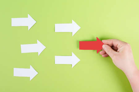 White arrows on a colored background, one red is standing out, do different, be a winner, individuality, making your own decision, leadership, target new ideの写真素材