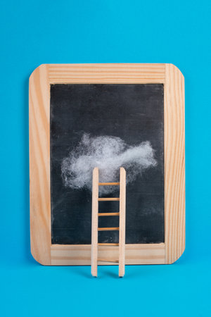 Ladder with a cloud on top, blank chalkboard, blue colored background, copy space, dreaming of success, creative and business concept, achieving new goalsの写真素材