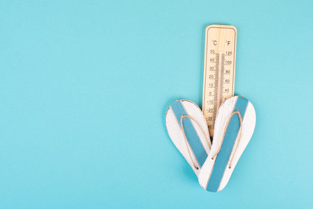 Empty blue background with a thermometer and flip flops, holiday background, summer vacation, hot...
