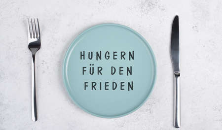 Starve for peace is standing in German language on the empty plate, food shortage because of the war in Ukraine, political issueの写真素材