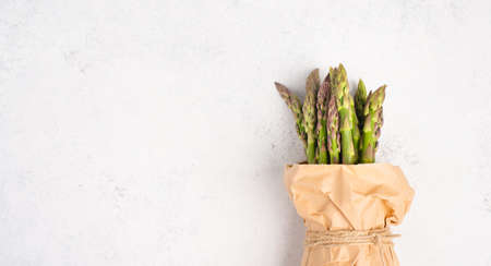 Fresh green bundle of asparagus on a white textured table, vegetables in spring, gourmet cuisine food, cooking a vegan mealの写真素材