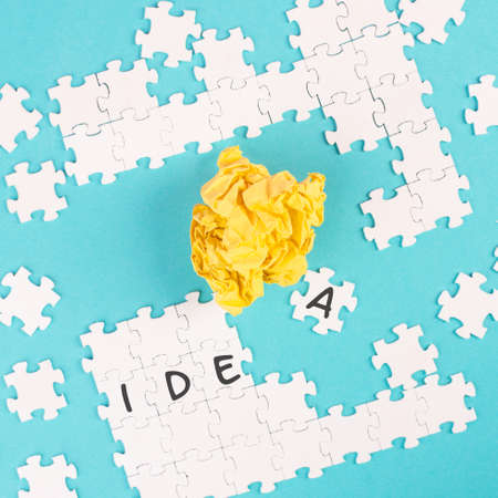 Puzzle on a blue background, yellow crumbled paper, word idea is standing on the jigsaw pieces, brainstoming concept, working as a team togetherの写真素材