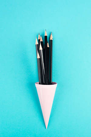 Black pencilsin a cone on a blue background, minimalism, creative, surreal and education concept, copy space for text, pastel colored wallの写真素材