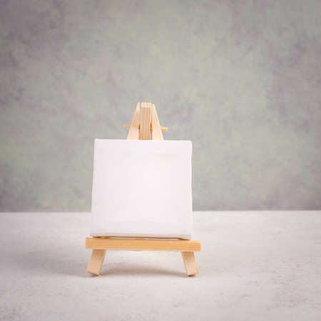Easel with blank white canvas in front of a gray textured background, frame to add paintings and picturesの写真素材