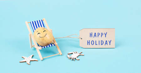 Potato with a funny face is sitting in lounge chairs, sign with the words happy holiday, greeting cardの写真素材