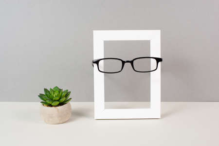 Home interior poster mock up with wooden frame, eyeglasses and cactus in a pot, gray wall background, copy space for text and picturesの写真素材