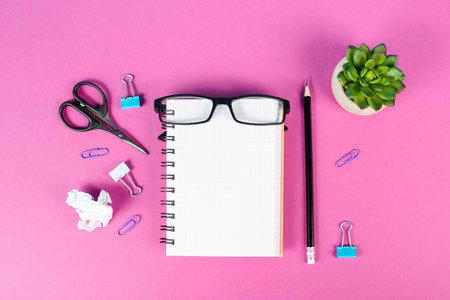 Empty notebook with a pen, eyeglasses and a cactus on a pink colored desk, brainstorming for new ideas, writing a message, home office workplaceの写真素材