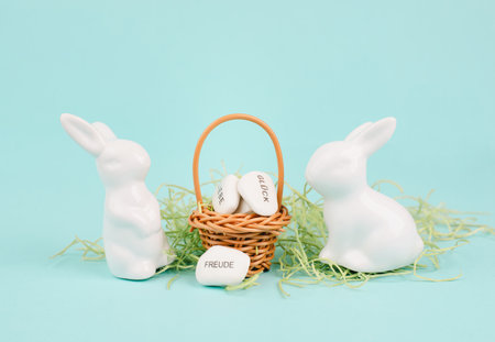 Wicker basket and easter bunny, words like love, luck and joy are standing in German language on the pebbles, rabbit brings gift and wishesの写真素材