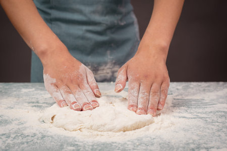 Baker kneading dough for pizza or artisan bread with his hands, preparing ingredients for food,...