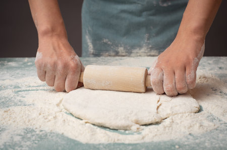 Baker rolls out dough for pizza, flatbread or pastry with rolling pin, prepare ingredients for food,...