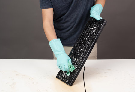Cleaning computer keyboard in office with rubber protective glove, whipping with water and soap, cleaning dusty and dirty electronics, houseworkの写真素材