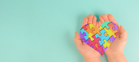 ASD autism spectrum disorder, deficits in social communication and interaction, hands holding heart with colorful jigsaw or puzzle piecesの写真素材