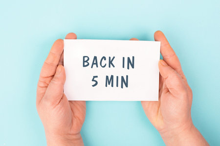 Back in 5 min is standing on a paper, hands hold message, working break, be right back