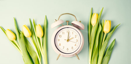 Alarm clock with yellow tulip flowers, switch to daylight saving time in spring, summer time changeoverの写真素材