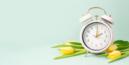 Alarm clock with yellow tulip flowers, switch to daylight saving time in spring, summer time...