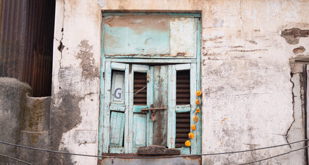 Old house in Mumbai, India, aged rustic facade with broken blue colored window, building with brick...