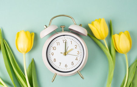 Alarm clock with yellow tulip flowers, switch to daylight saving time in spring, summer time...
