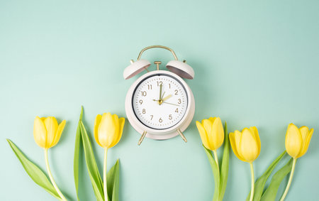 Switch to daylight saving time in spring, summer time changeover, alarm clock with yellow tulip...