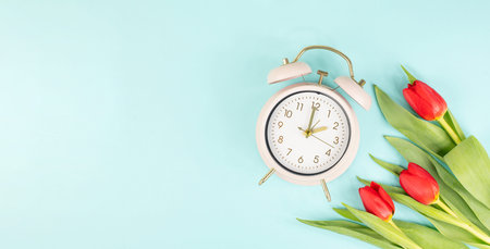 Switch to daylight saving time in spring, summertime changeover, alarm clock with red tulip flowers