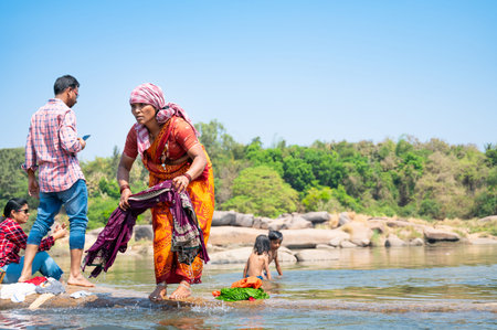 Indian woman washing clothes at Tungabhadra river, Hampi, colorful fabrics, traditional bangles on...