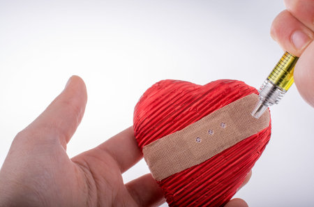 Hand injecting love into  heart  in plaster on white background