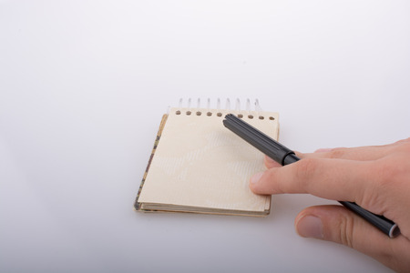 Hand holding a pen on a notebook on a white backgroundの写真素材