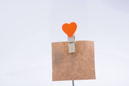 Heart shape clothespin attached to a note paper on a white backgroundの写真素材
