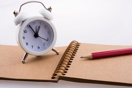 Color pencil and an alarm clock placed on a spiral brown notebook