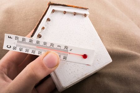 Hand holding a thermometer on a model houseの写真素材