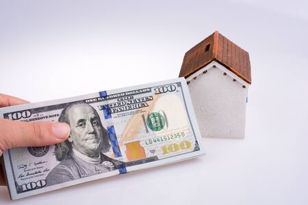 Human hand holding American dollar banknotes by the side of a model house on white backgroundの写真素材