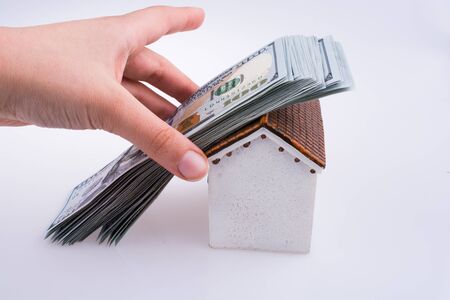 Hand holding American dollar banknotes on the roof of a model house  on white backgroundの写真素材